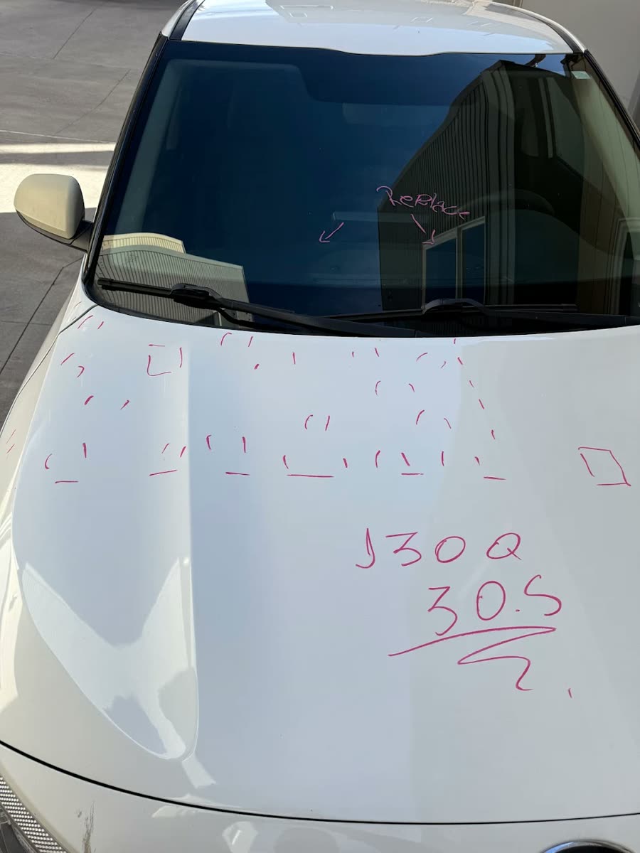 Real photo: a white hood with every hail dent marked in marker and the count written on the panel