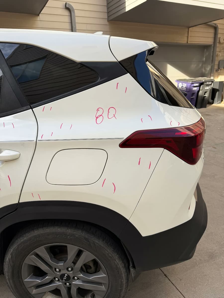 Real photo: the rear quarter of a white SUV with hail dents marked in marker
