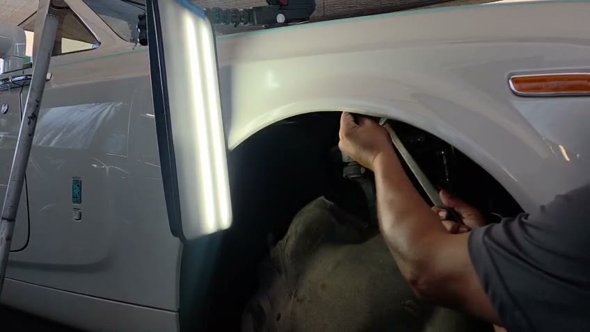 Real photo: a technician reaching behind a fender through the wheel well